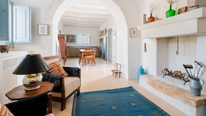 A spacious living room with a sofa, a coffee table, and a fireplace. There is a kitchen in the background with wooden cabinets and a dining area. - Ker Rail Villa With Pool by Wonderful Italy (Ostuni)