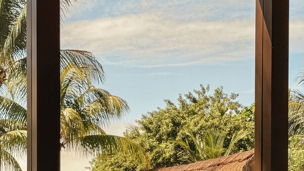 A breakfast table with croissants, a fruit platter, and a glass of juice, overlooking a pool area with a thatched-roof structure and palm trees. - Obi Exclusive Pousada (Maragogi)