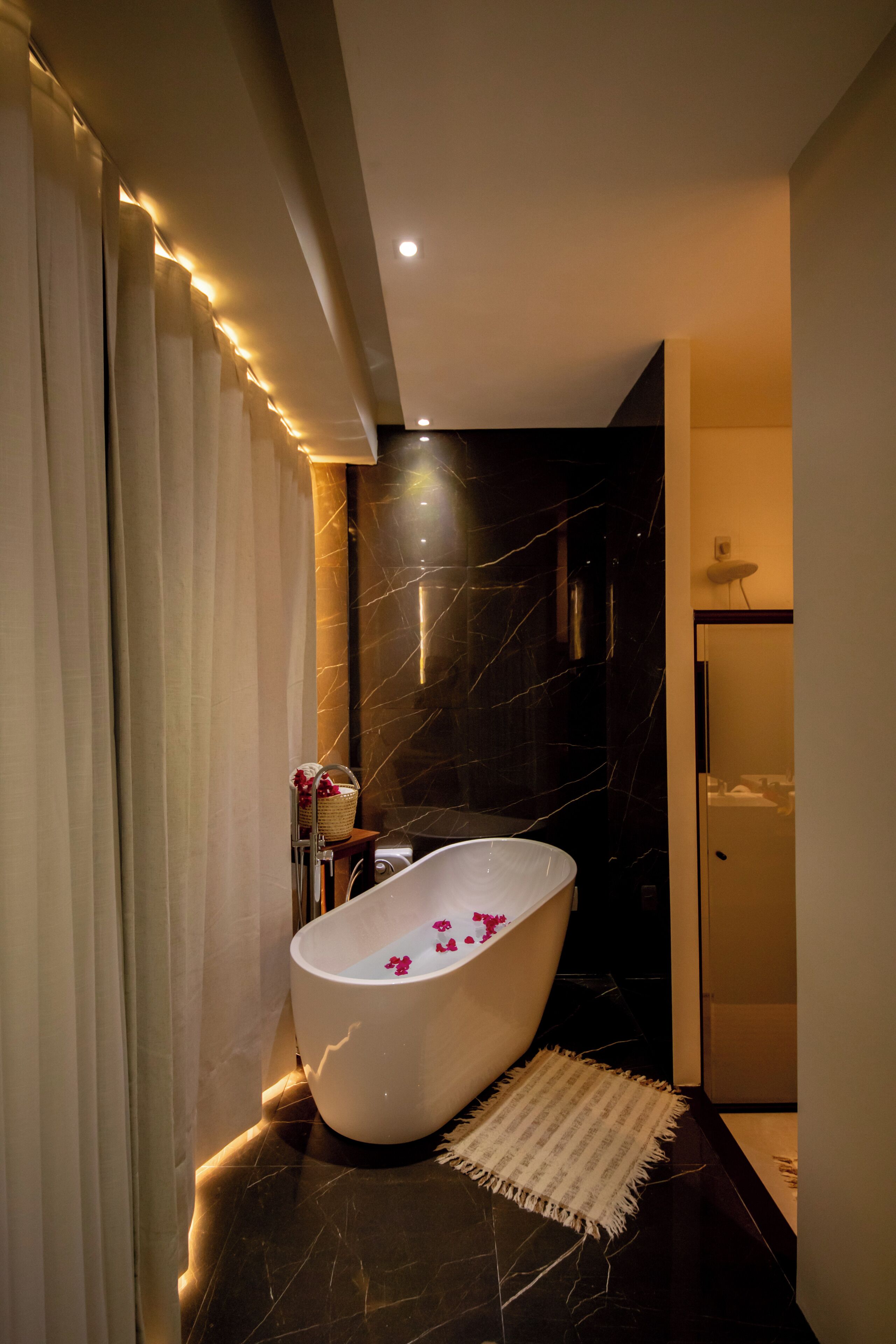 Ein modernes Badezimmer mit freistehender Badewanne, Marmorwänden und einem kleinen Teppich.