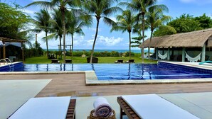 A poolside area with lounge chairs, a thatched-roof structure, and a view of the sea. - Obi Exclusive Pousada (Maragogi)