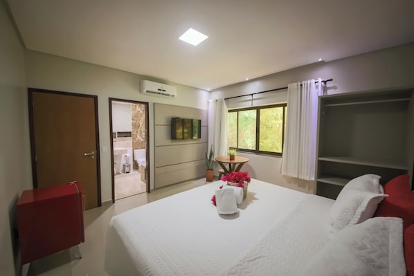 A hotel room with a bed, a red cabinet, a small table with flowers, a TV, and a window with curtains. - Obi Exclusive Pousada (Maragogi)
