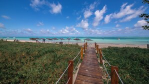 A wooden pathway leading to a beach with umbrellas and lounge chairs. - Obi Exclusive Pousada (Maragogi)