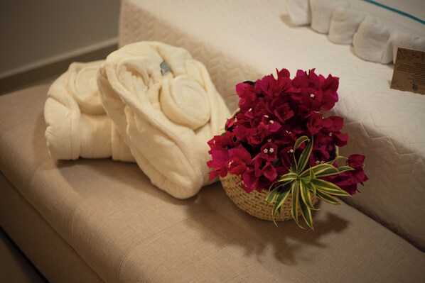 A neatly made bed with a rolled white towel and a basket of red flowers.