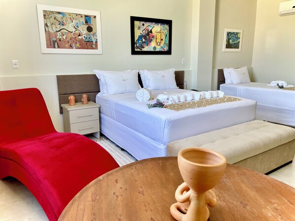 A hotel room with two beds, a red chair, a wooden table with a cup, and artwork on the walls. - Obi Exclusive Pousada (Maragogi)
