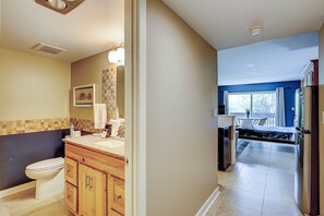 Ein modernes Badezimmer mit Toilette, Waschtisch und Waschbecken. Ein Flur führt zu einem Schlafzimmer mit Bett und Blick ins Freie.