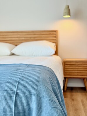 A neatly made bed with a blue blanket, a wooden headboard, and a bedside table with a lamp. - Beautiful 2-bedroom apartment in Figueira da Foz (Figueira da Foz)