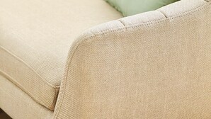 Ein beiges Sofa mit zwei hellgrünen Kissen und einer braunen Quaste.