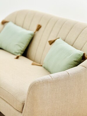 A beige sofa with two light green pillows and a brown tassel detail. - Beautiful 2-bedroom apartment in Figueira da Foz (Figueira da Foz)