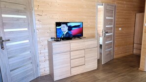 Une pièce aux murs et au plancher en bois, avec un téléviseur posé sur un meuble en bois et deux portes en bois.