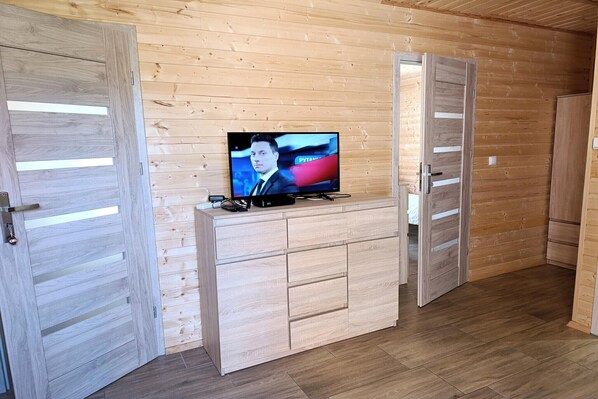 A room with wooden walls and floors, a TV on a wooden cabinet, and two wooden doors.