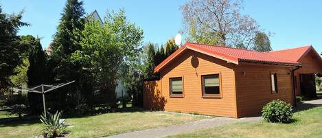 Une cabane en bois avec un toit rouge, entourée d’une cour verdoyante et d’arbres.