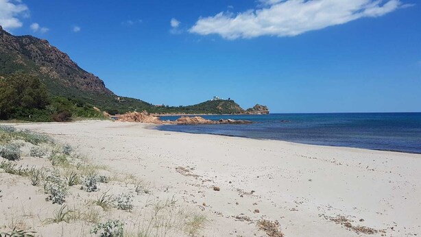 En strand med vit sand, en klippformation och en klarblå himmel.