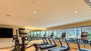 Une salle de sport équipée de tapis de course, de vélos d’exercice et d’un écran de télévision.