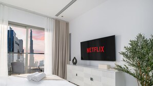 Une chambre d’hôtel moderne dotée d’une grande fenêtre donnant sur le paysage urbain, d’un téléviseur à écran plat et d’un lit parfaitement fait.