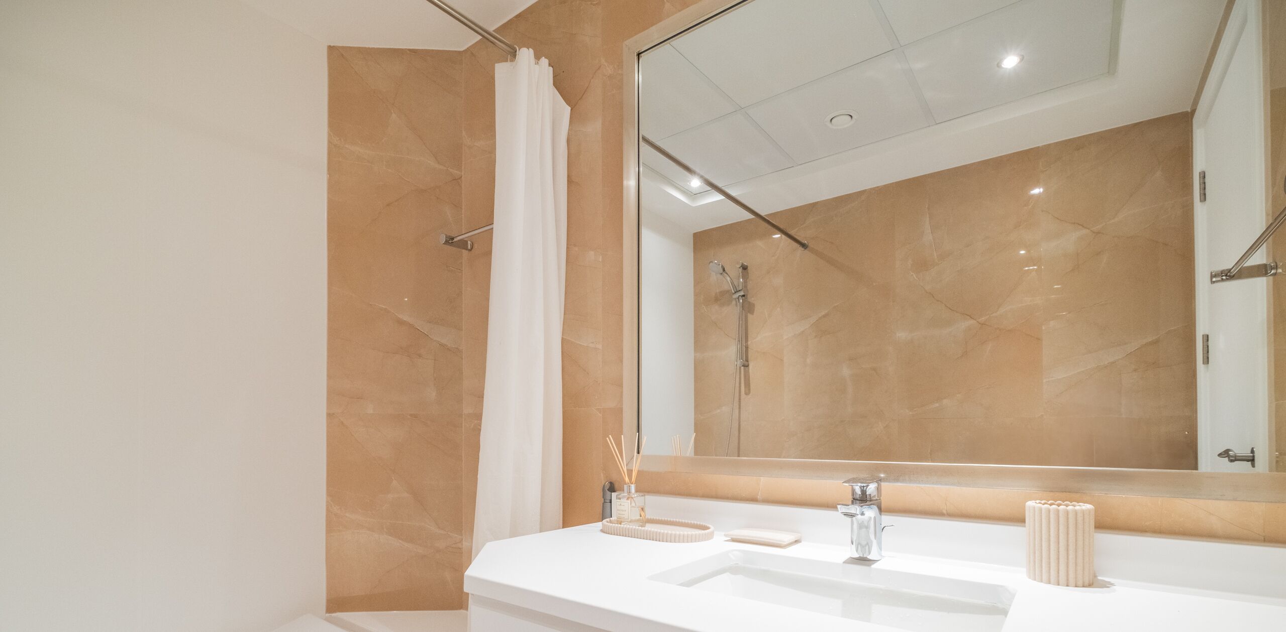 A modern bathroom with a large mirror, a shower, and a vanity with two sinks.