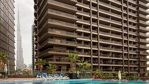 Un immeuble de grande hauteur doté de nombreux balcons, d’une piscine avec des chaises longues et de palmiers.