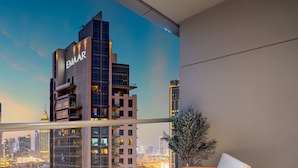 Un bâtiment moderne dont la façade porte l’inscription « EMMAAR », vu de l’intérieur d’une pièce dotée d’un balcon donnant sur un paysage urbain au crépuscule.