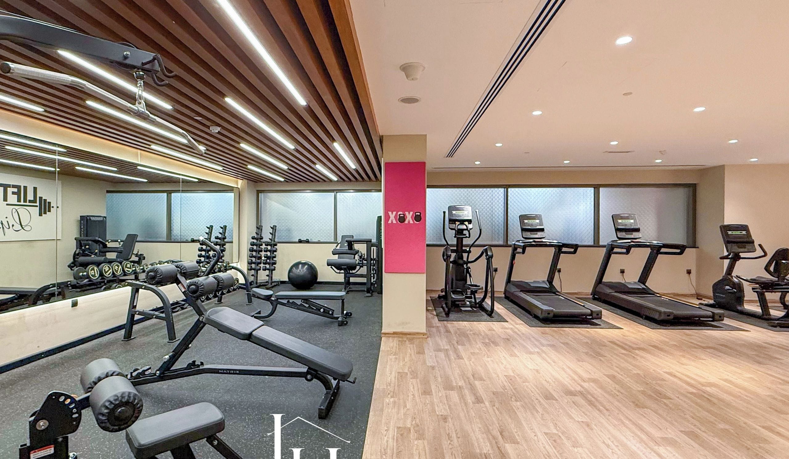Une salle de sport moderne équipée de divers appareils d’exercice, notamment des tapis de course et des appareils de musculation, et dotée d’un plancher en bois.