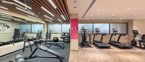 Une salle de sport moderne équipée de divers appareils d’exercice, notamment des tapis de course et des appareils de musculation, et dotée d’un plancher en bois.