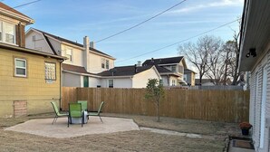 A backyard with a concrete patio, two green chairs, a small tree, and a wooden fence. - Charming 2-bedroom studio with WiFi, AC in the heart of downtown Bartlesville (Bartlesville)
