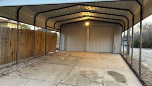 A covered garage with a metal roof, a concrete floor, and a wooden fence in the background. - Charming 2-bedroom studio with WiFi, AC in the heart of downtown Bartlesville (Bartlesville)