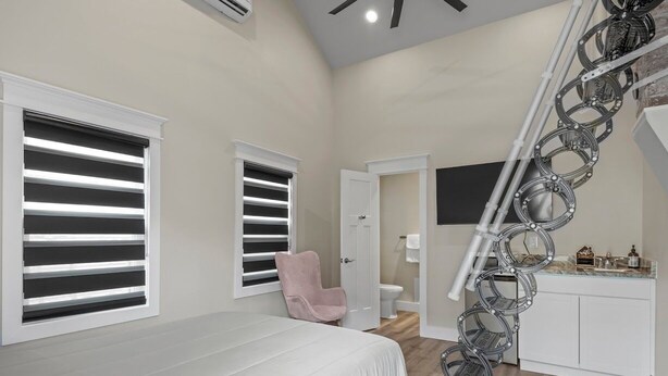 A bedroom with a bed, two windows with blinds, a pink chair, a staircase, and a bathroom visible in the background. - Charming 2-bedroom studio with WiFi, AC in the heart of downtown Bartlesville (Bartlesville)
