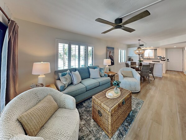 A spacious living room with a sofa, armchairs, a coffee table, and a dining area with a table and chairs. - Seaside 410 | Newly Updated Corner Condo w/Gulf Views (Fort Myers Beach)