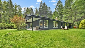Una casa moderna con un porche cubierto, césped y un fondo de bosque.