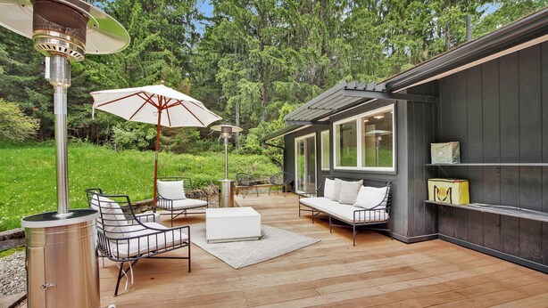 Una terraza de madera con mobiliario exterior, una parrilla y un gran paraguas.