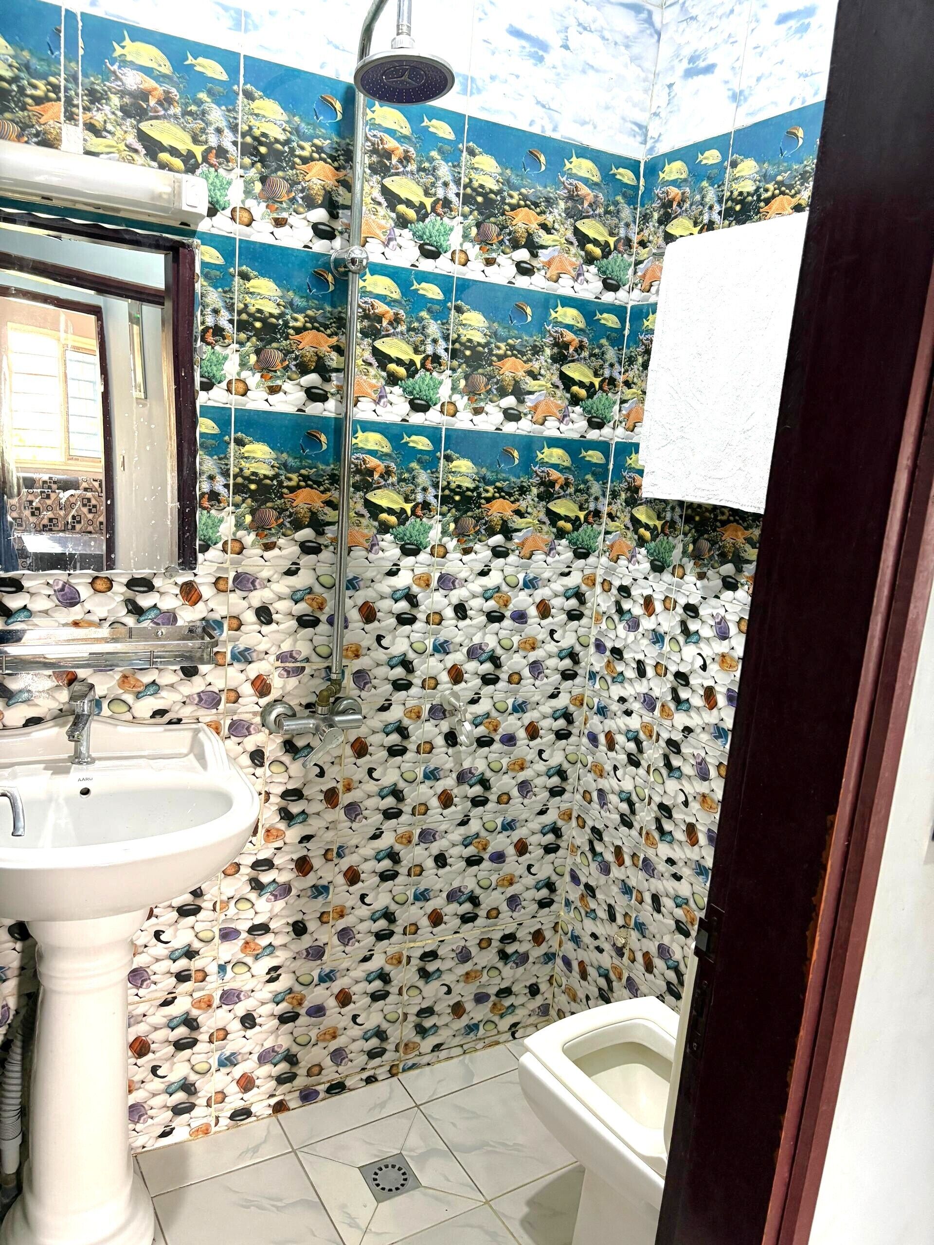 Een badkamer met een wastafel, toilet en douche. De wanden zijn versierd met een mozaïek van verschillende stenen en schelpen.