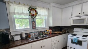 Una cocina con armarios blancos, encimera de madera, un lavabo, un microondas y una estufa.