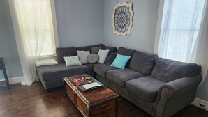 Una sala de estar con un sofá seccional gris, una mesa de centro de madera y un adorno de pared.