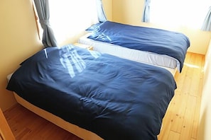 Quarto com duas camas, piso de madeira e janela com cortinas.