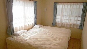 Een slaapkamer met een groot bed, twee ramen met gordijnen en een houten vloer.