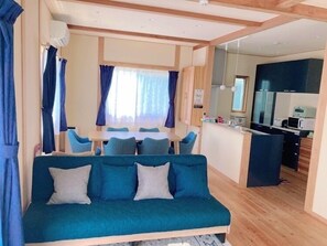 Uma sala de estar aconchegante com sofá, mesa de jantar e cadeiras. Possui uma cozinha compacta com micro-ondas e geladeira.