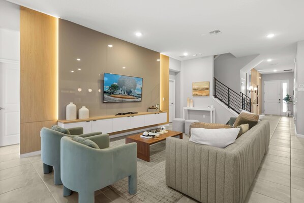 A modern living room with a sofa, chairs, a coffee table, and a TV mounted on the wall.