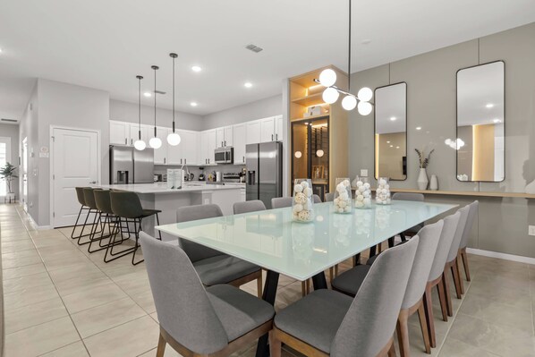 A modern kitchen with white cabinets, stainless steel appliances, and a dining area with a glass table and grey chairs.