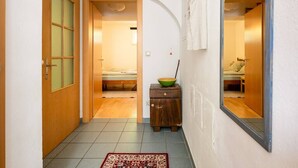 A narrow hallway with a wooden door, a small wooden cabinet with a bowl, and a mirror reflecting a bed. - Central, quiet oasis with garden and parking lot (Graz)