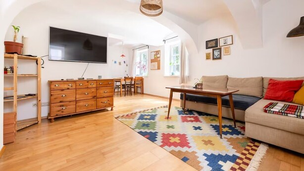 A spacious living room with a wooden cabinet, a sofa, a coffee table, and a TV mounted on the wall. - Central, quiet oasis with garden and parking lot (Graz)