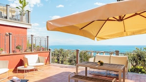 Una terraza con mesa, sillas y sombrilla, con vistas panorámicas al mar.