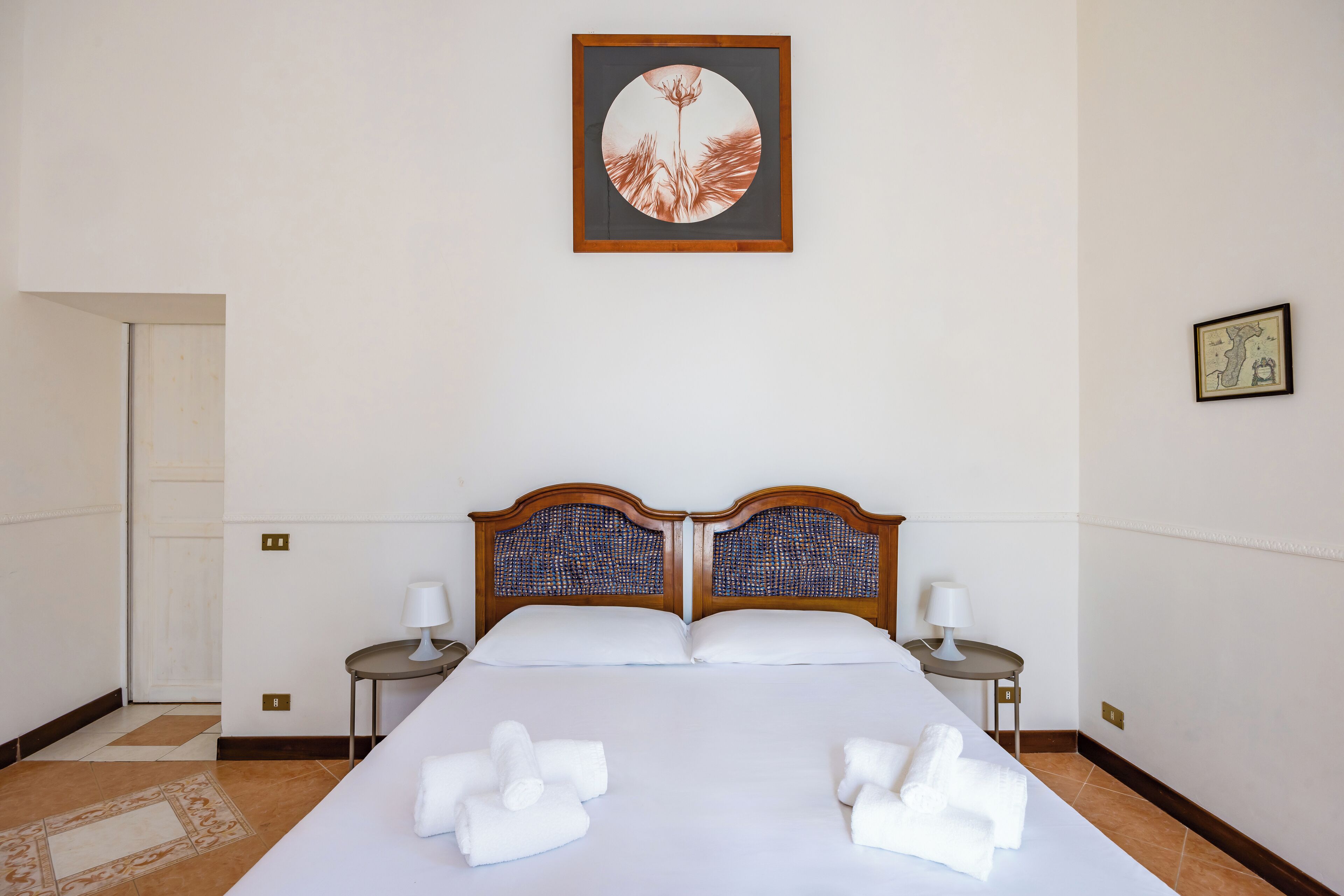 A hotel room with a large bed, two bedside tables with lamps, a framed artwork above the bed, and a small framed picture on the wall.