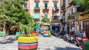A narrow street with colorful planters, parked scooters, and a building with balconies. - La Casa di Famiglia by Napoliapartments (Naples)