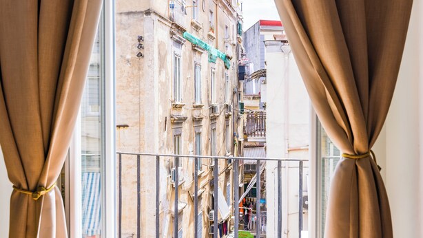 A view through curtains of a building with multiple balconies and a visible fire escape. - La Casa di Famiglia by Napoliapartments (Naples)