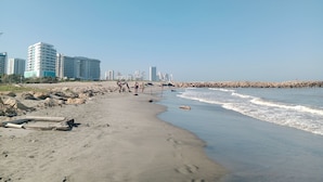 Una playa con costa rocosa, algunas personas y edificios altos al fondo.