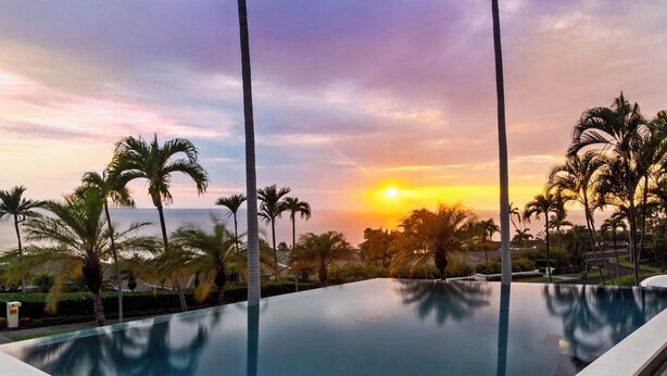 Una piscina con vista al atardecer, rodeada de palmeras.