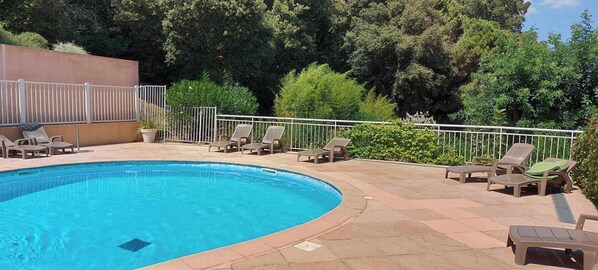 Una piscina con sillones de descanso y una valla de metal.