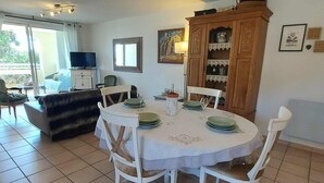 A dining area with a round table set for four, surrounded by white chairs. There is a cabinet with decorative items and a painting on the wall.