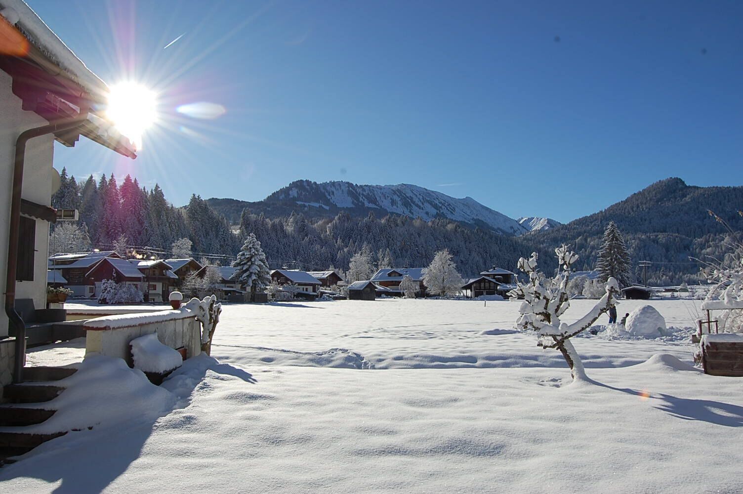 A snow-covered village with traditional wooden houses, a clear sky, and mountains in the background.