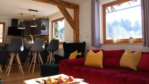 Ein gemütliches Wohnzimmer mit einer roten Couch, Holzbalken und einem Essbereich mit Stühlen und einem Tisch.
