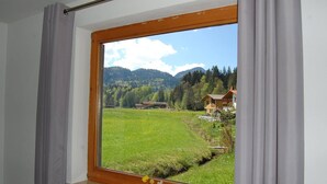 Ein Zimmer mit großem Fenster mit Blick auf ein grünes Feld und eine Berglandschaft.
